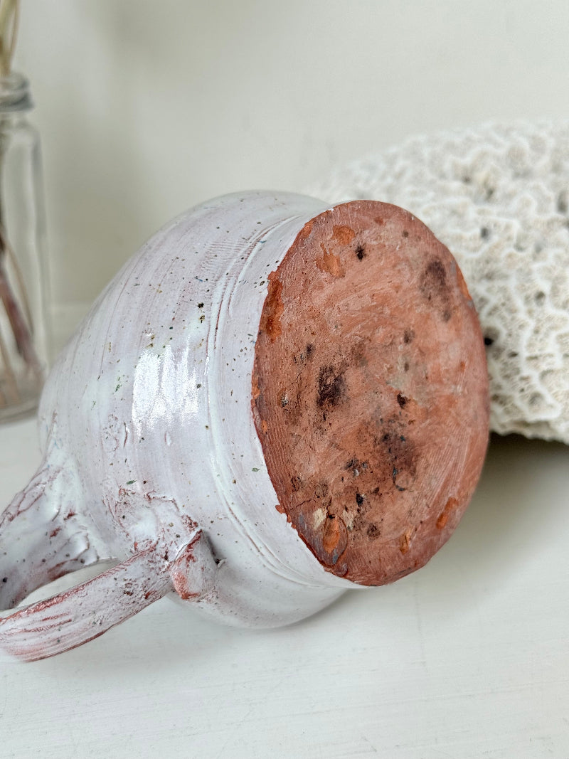 Studio pottery milk jug with soft pink and grey speckled glaze, photographed on a white surface