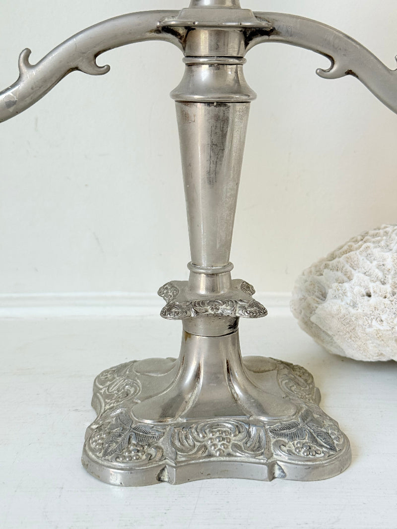 Vintage silver coloured three-arm candelabra with ornate base and soft patina, photographed on a white surface