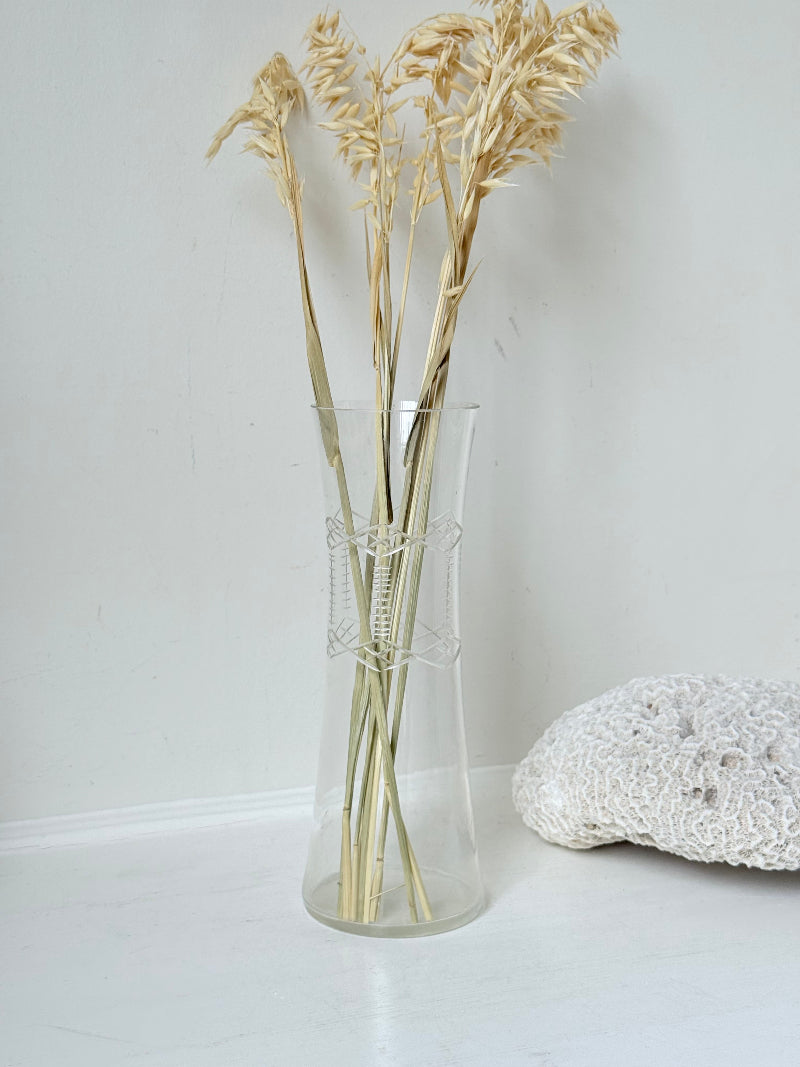 Vintage clear glass cylinder vase with etched leaf design, photographed on a white surface.
