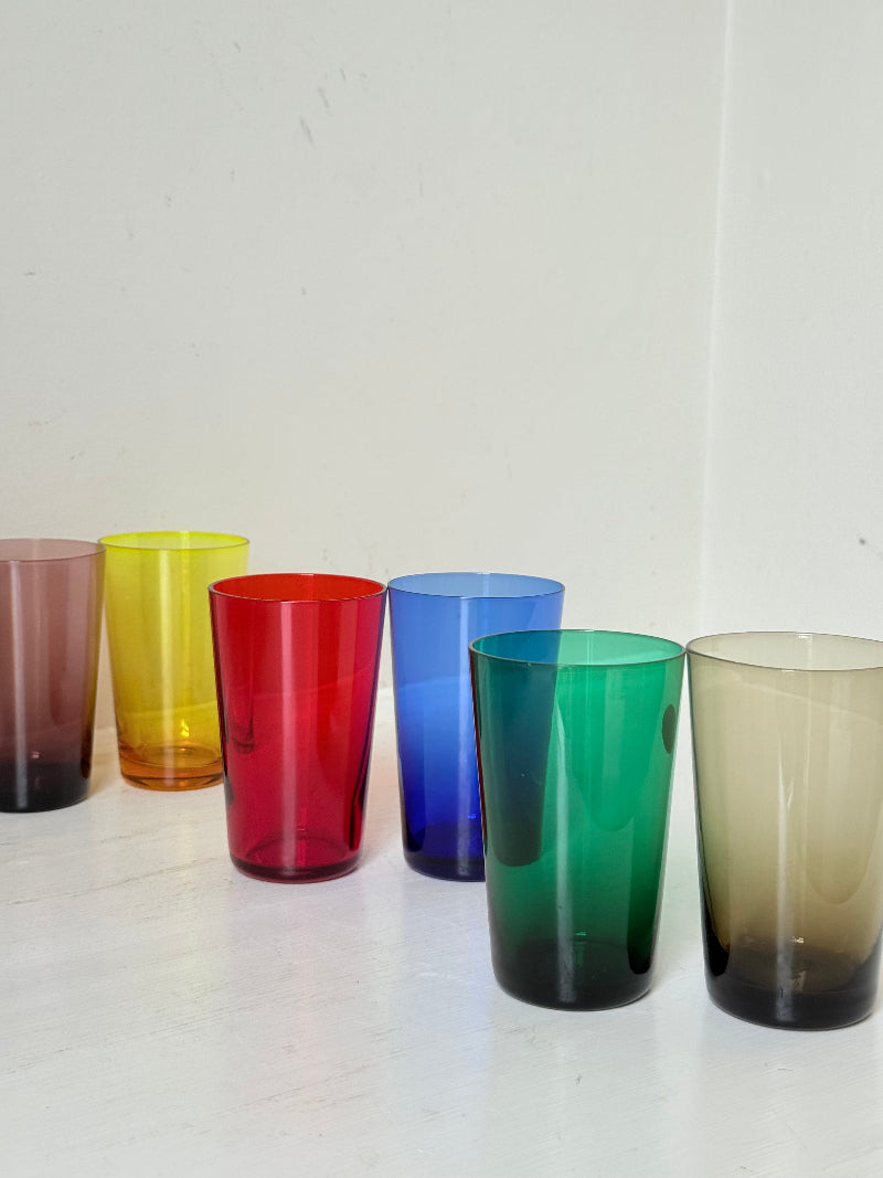 Set of six mid-20th century Boussu coloured glass beakers in rainbow hues, green with original label, photographed on white surface.