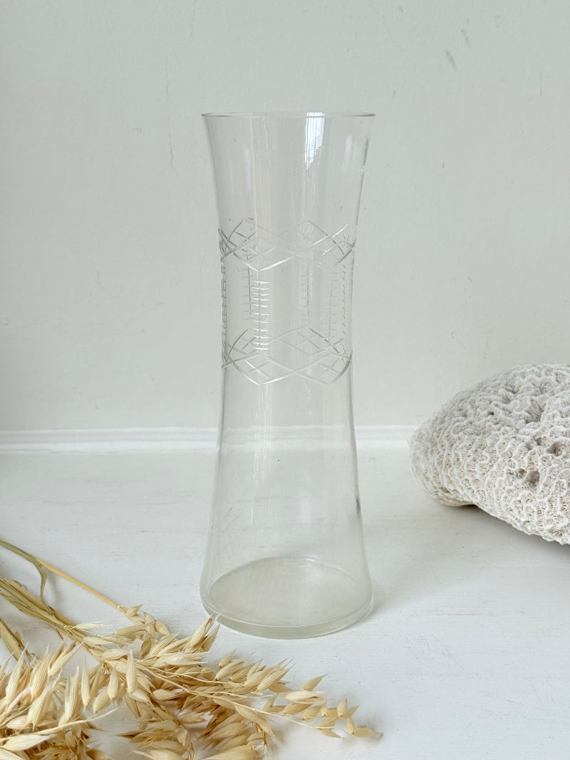Vintage clear glass cylinder vase with etched leaf design, photographed on a white surface.