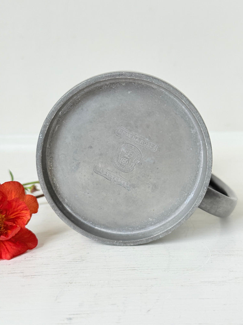 vintage pewter tankard with crown and rose mark and handle, styled with red and orange flowers on white surface