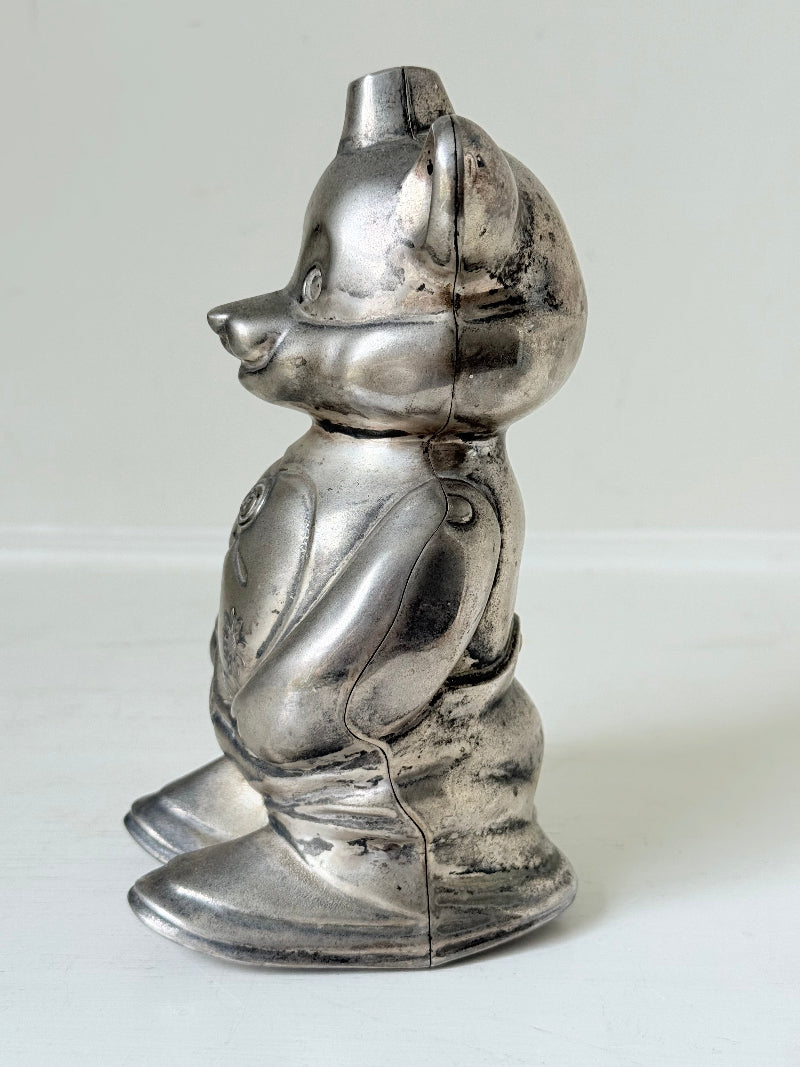 Vintage silver tone metal bear money box with coin slot on top, photographed on a white surface.