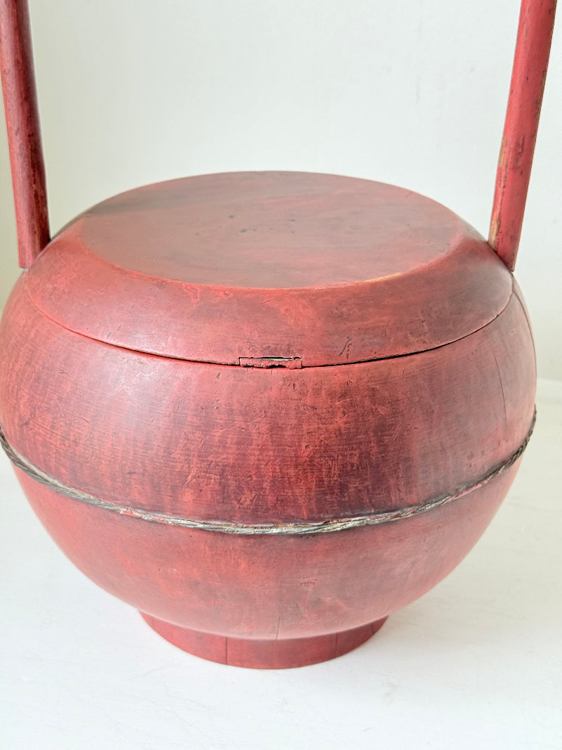 Vintage red painted wooden basket with tall curved handle and domed lid photographed on a white surface