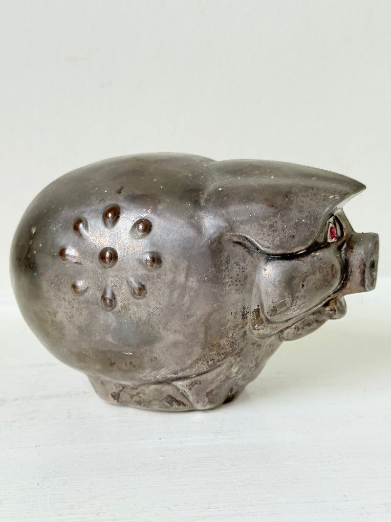 Vintage cast metal piggy bank in the shape of a pig with red painted eyes, photographed on a white surface