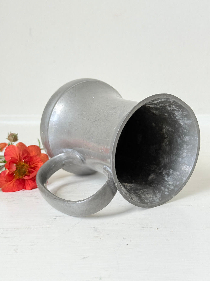 vintage pewter tankard with crown and rose mark and handle, styled with red and orange flowers on white surface