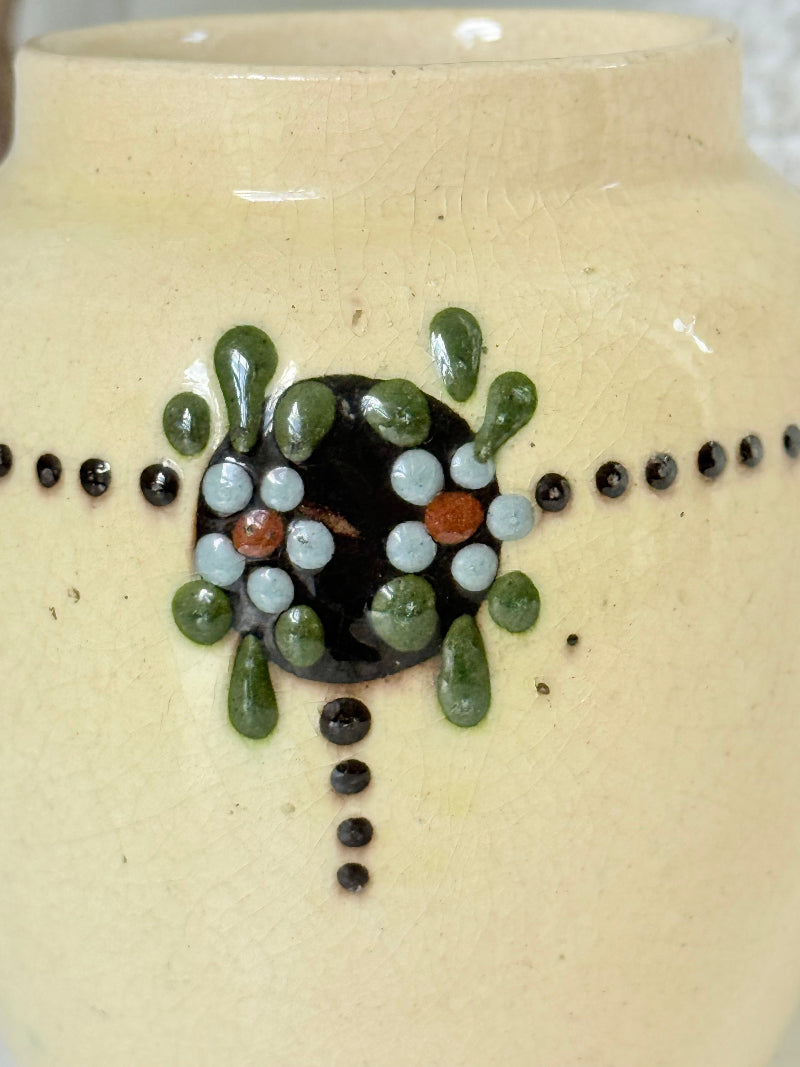 Cream studio pottery decorative pot with raised green floral motif, photographed on a white surface