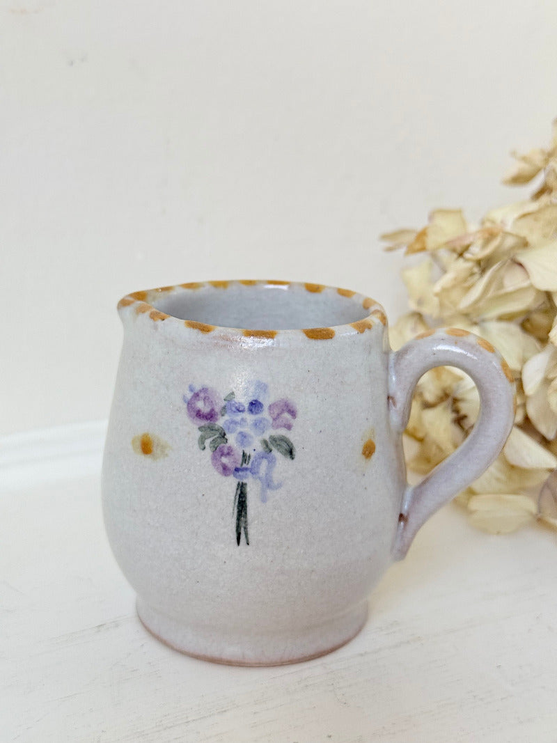 vintage studio pottery milk jug with hand painted lilac flowers and ochre rim photographed on white surface