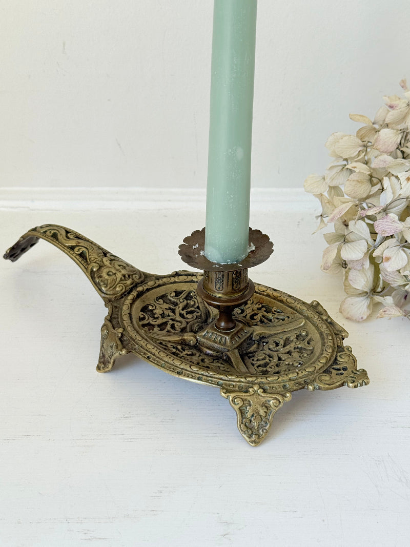 Ornate vintage brass candlestick with decorative handle and footed base, photographed on a white surface