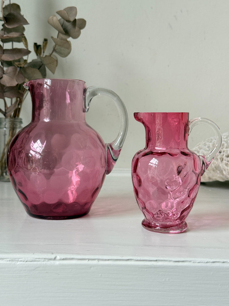 Vintage cranberry glass jugs, a pair with clear handles, photographed on a white surface