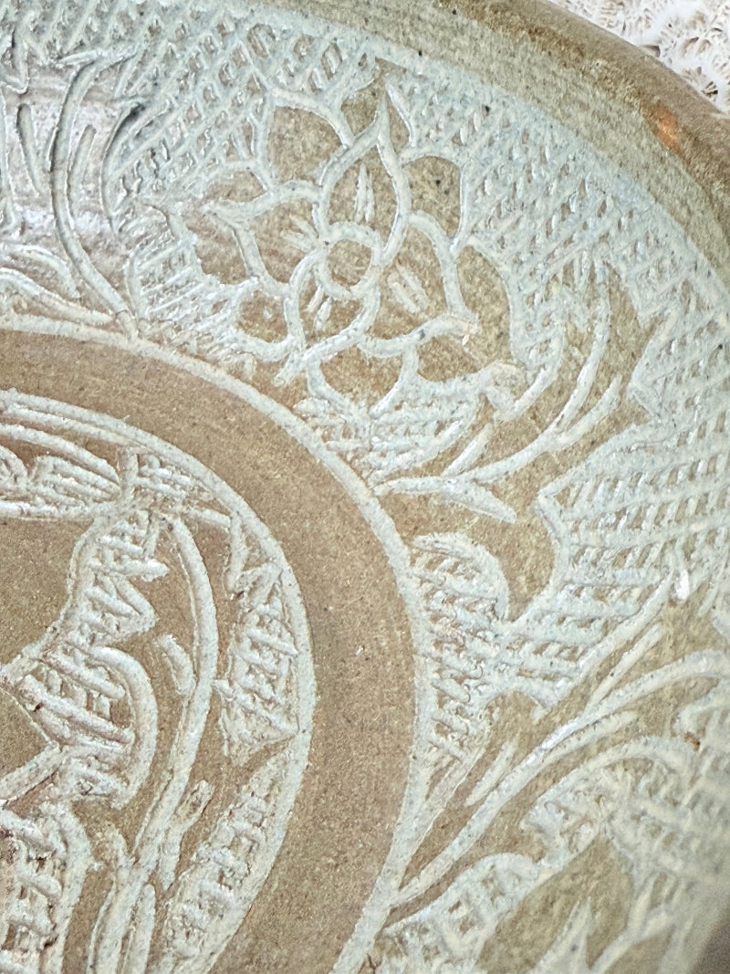 Studio pottery bowl with carved floral and geometric decoration in neutral glaze, photographed on a white surface with a pear inside.