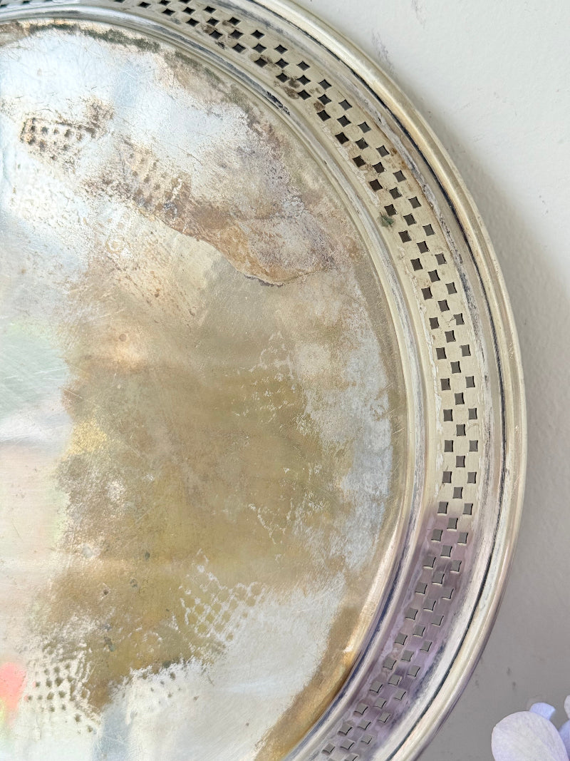 Vintage round silver plate tray with brass rim, pierced edge and etched central motif, photographed on white surface