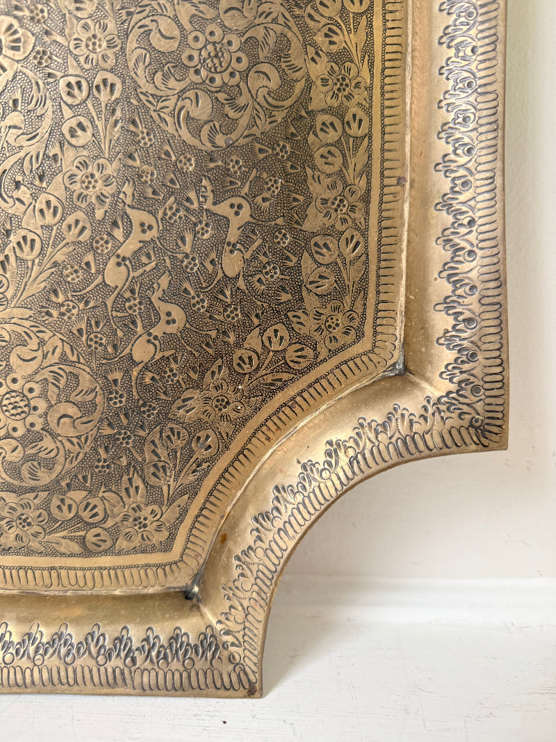Vintage hand engraved brass wall plaque with floral scrollwork, figural decoration, shaped edge and aged patina