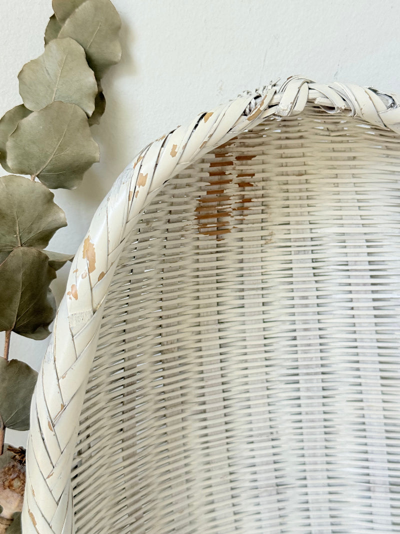 Vintage white chippy wicker basket with oval shape and worn painted finish, photographed on white surface.