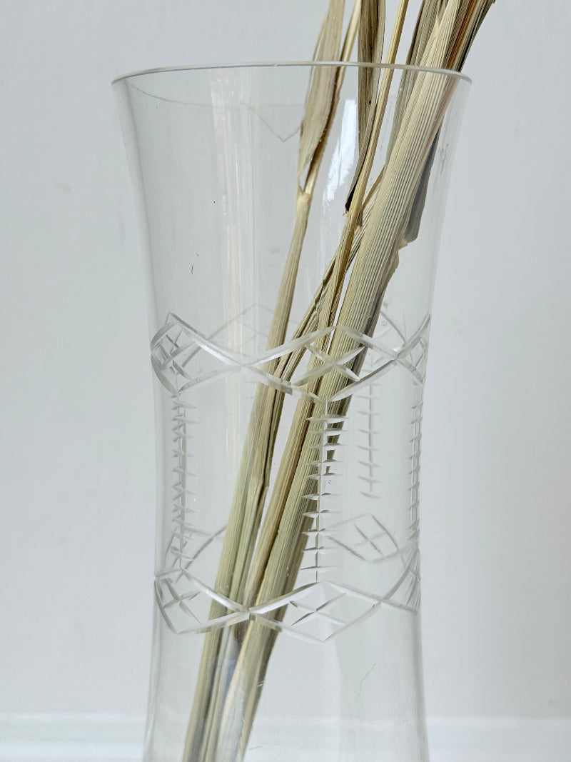Vintage clear glass cylinder vase with etched leaf design, photographed on a white surface.