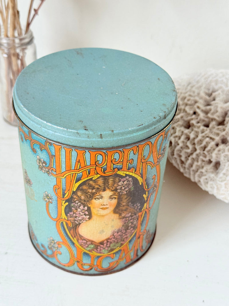 Vintage turquoise and gold metal sweet tin with Art Nouveau woman portrait photographed on a white surface.