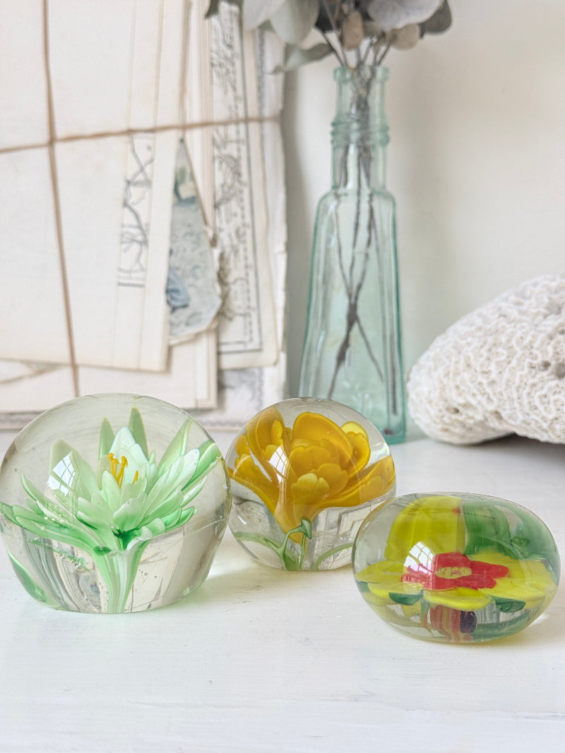 Trio of mixed flower glass paperweights in green, yellow and red, graduated in size, photographed on a white surface