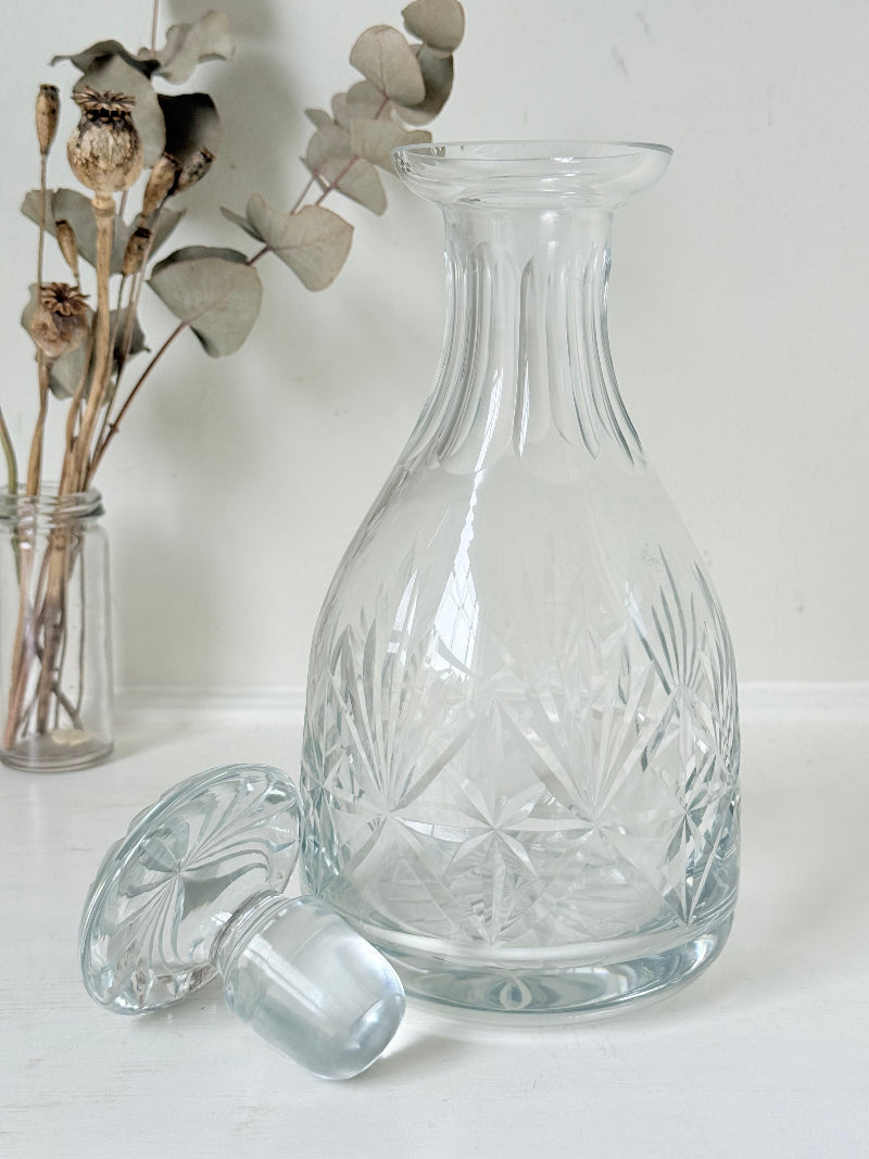 Vintage crystal decanter with faceted stopper and cut glass starburst design, photographed on a white surface