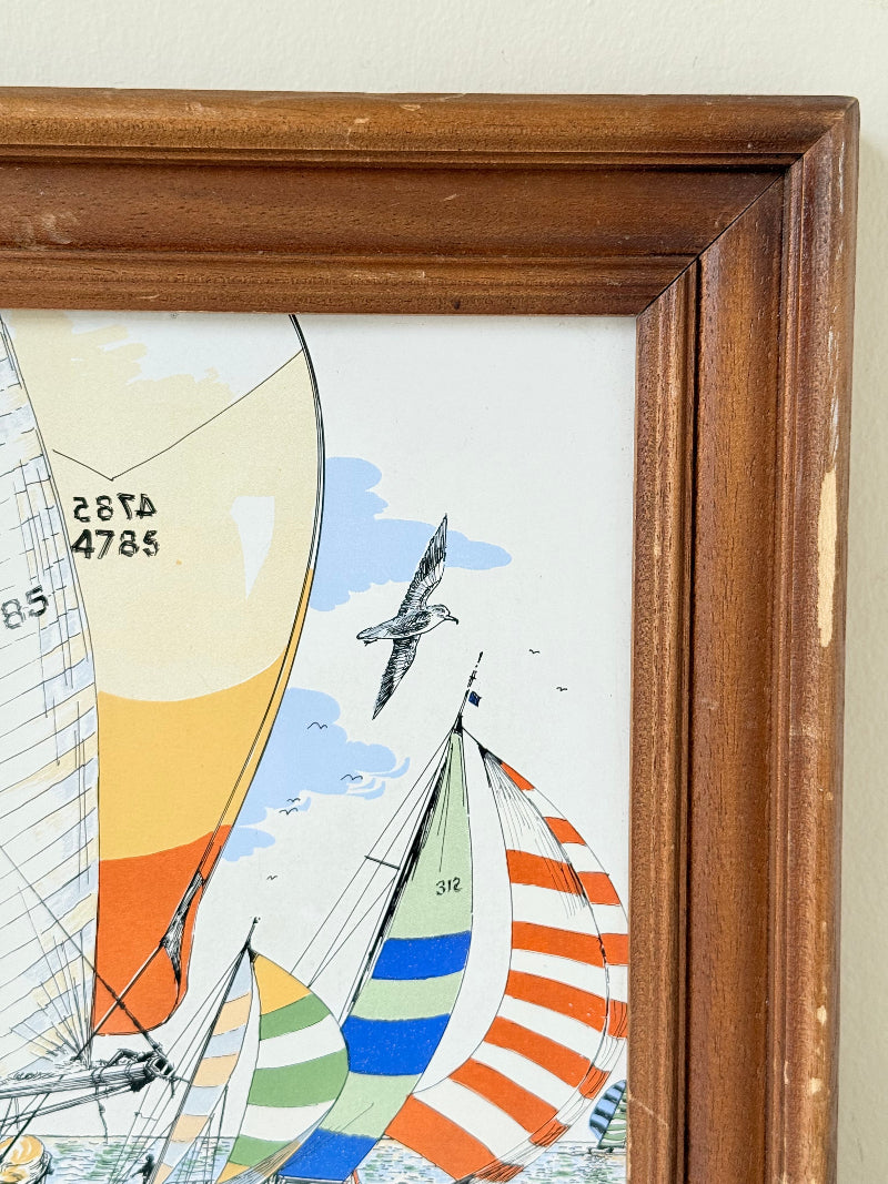 Vintage enamel artwork of sailing yachts with colourful striped sails in a regatta, framed in wood, photographed on white surface.