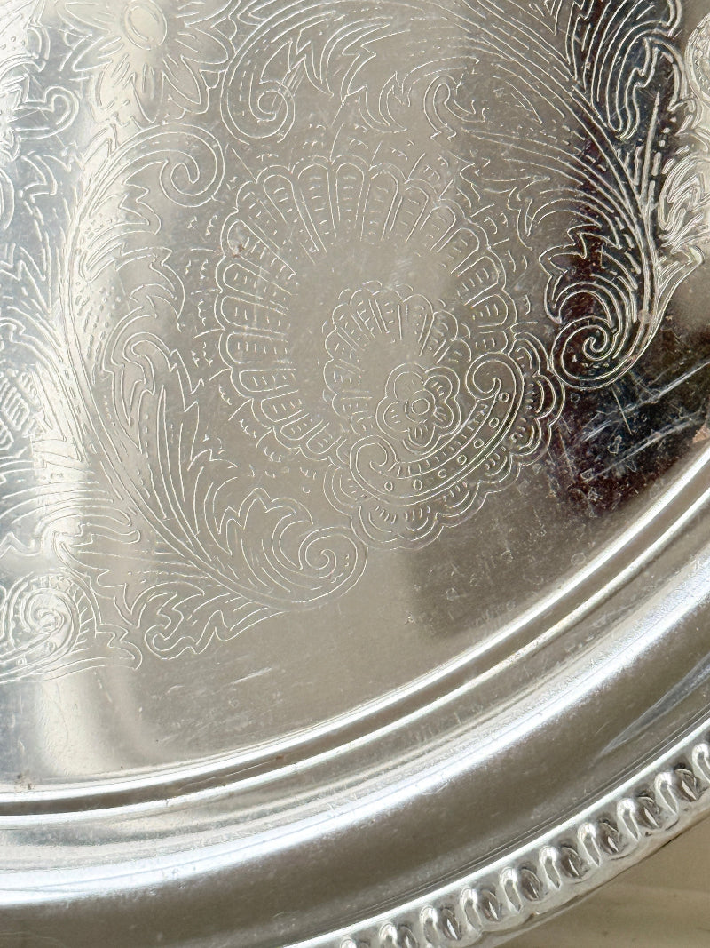 Vintage silver tone round tray with beaded edge, engraved surface detail and reflective finish for drinks or vanity styling
