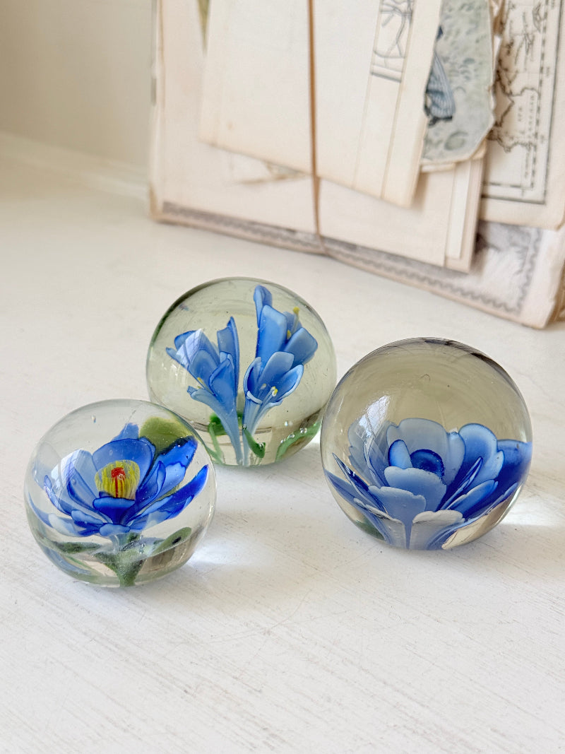 Trio of vintage glass paperweights with hand worked blue floral detail, clear glass domes and green leaf decoration