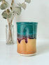 Studio pottery pen pot with teal and plum drip glaze, photographed on a white surface