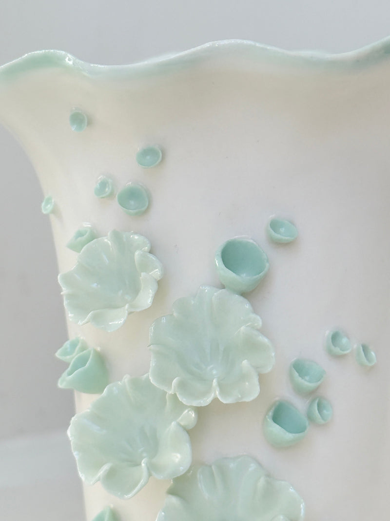 White Chessell Pottery studio vase with rippled rim and raised aqua floral decoration photographed on a white surface
