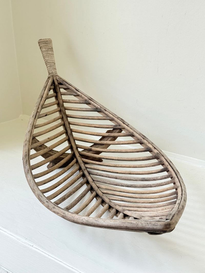 Large curved woven basket with slatted sides and repaired plywood base photographed on a white surface