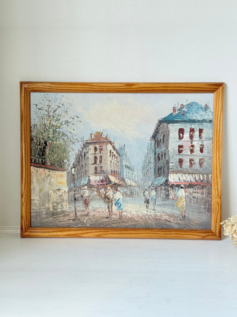 Vintage oil painting of European street scene with buildings and awnings in wooden frame photographed on a white surface