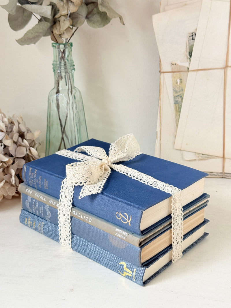 Bundle of vintage blue cloth books with gilt spines tied with ivory lace ribbon for shelf and table styling