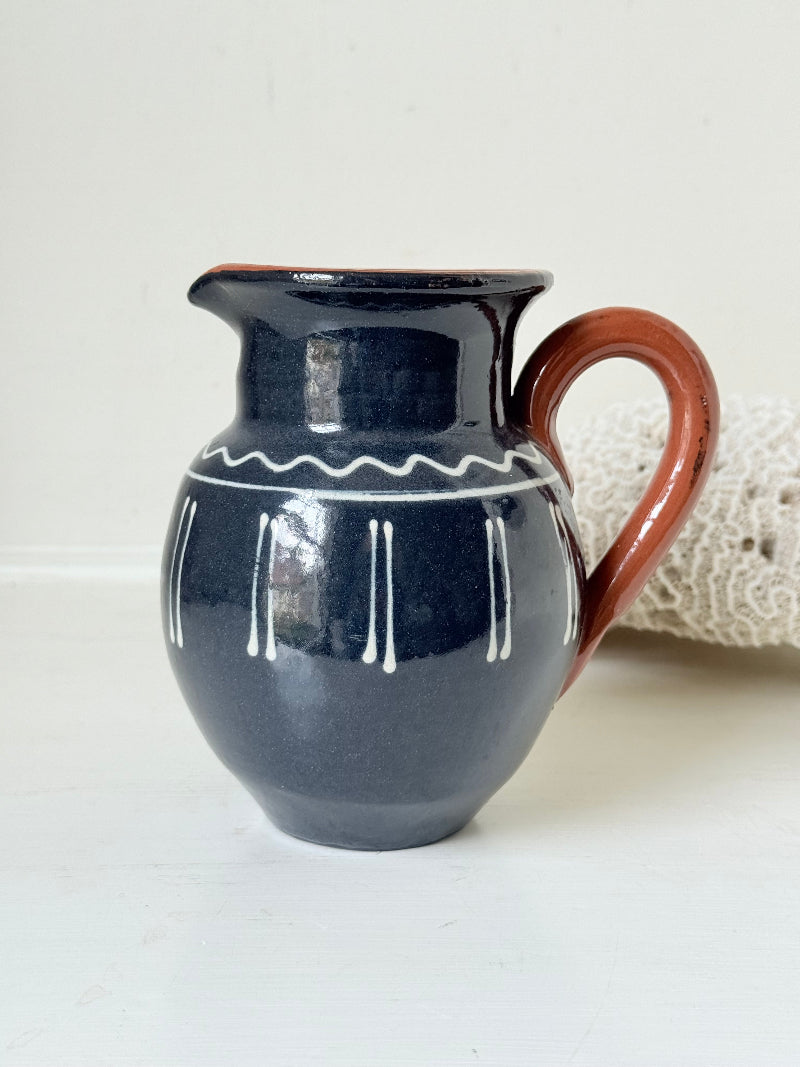 Slipware studio pottery jug with blue glaze and terracotta handle, photographed on a white surface