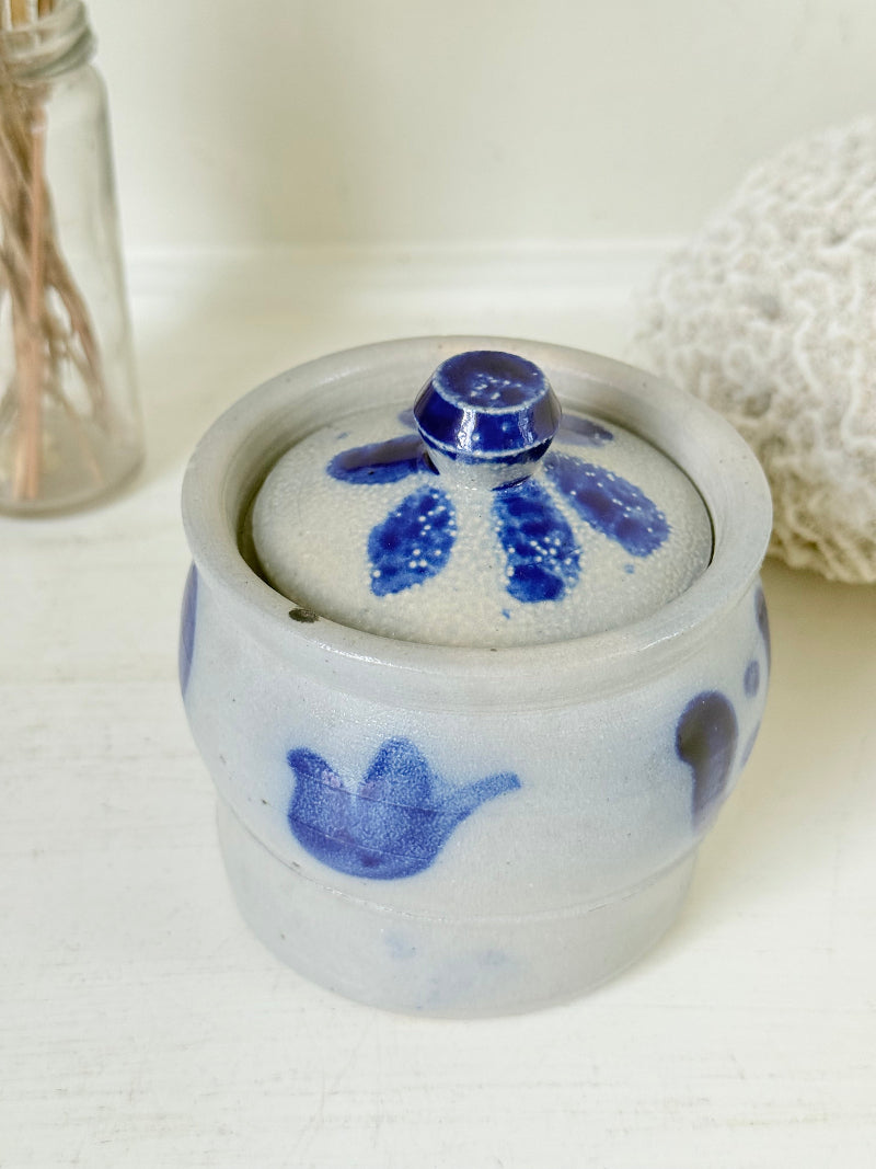 Vintage lidded pottery jar with hand painted blue floral decoration, photographed on a white surface