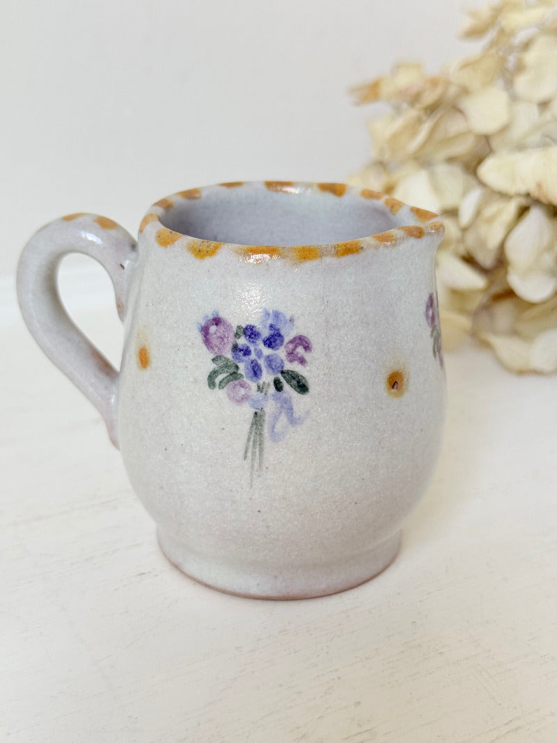vintage studio pottery milk jug with hand painted lilac flowers and ochre rim photographed on white surface