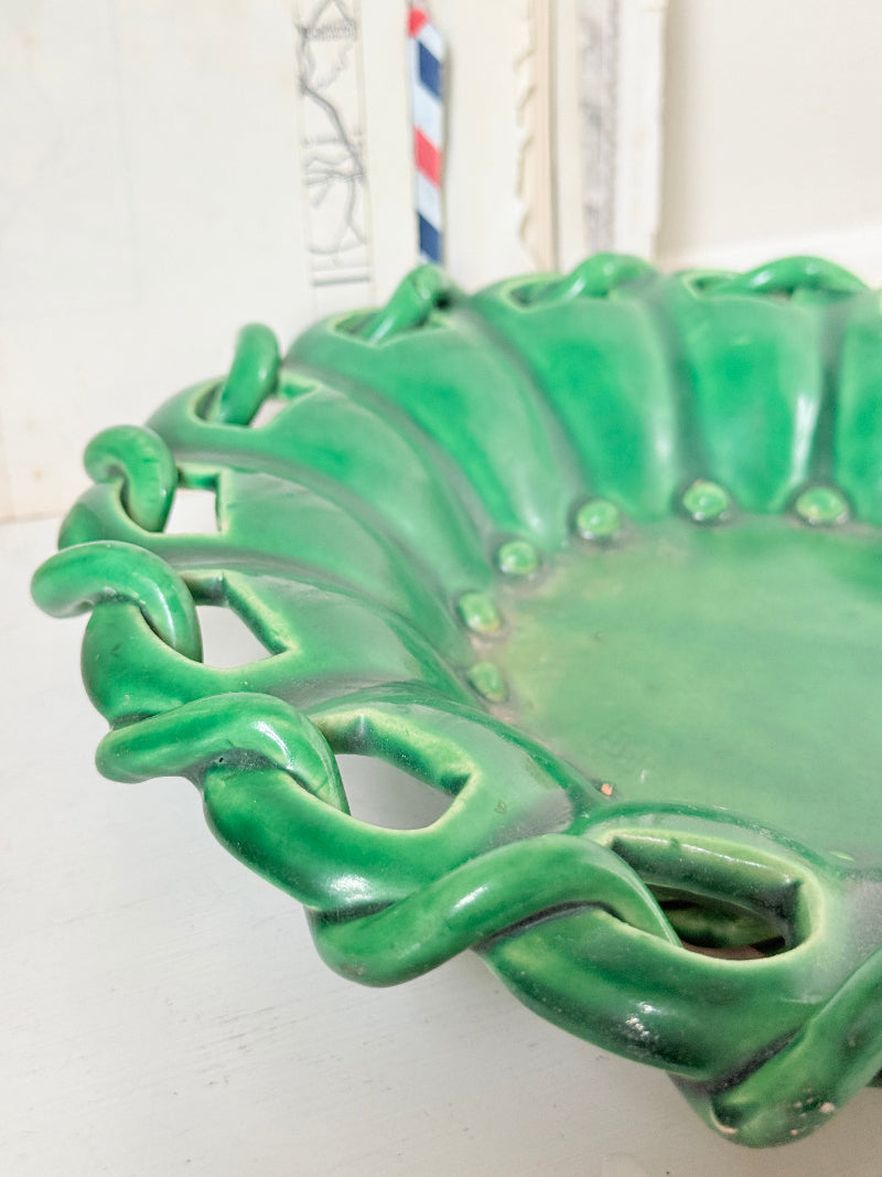 A glossy green ceramic bowl with a decorative wavy rim and openwork details, photographed close-up on a light surface.