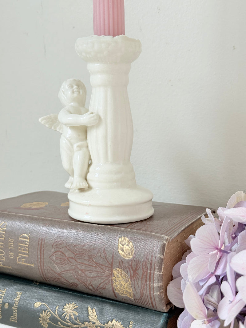 Vintage ceramic candlestick with angel figure and fluted column, cream glazed, styled with pink candle on white surface
