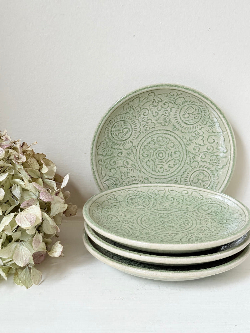 Set of four Thai celadon side plates with embossed patterns and sage green crackled glaze, stacked and photographed on white surface