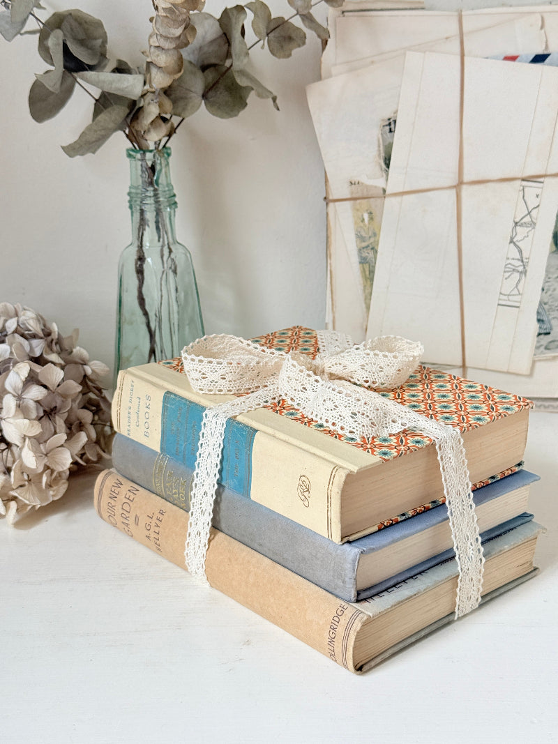 Bundle of vintage cream and blue cloth books with one patterned cover tied with ivory lace for shelf styling