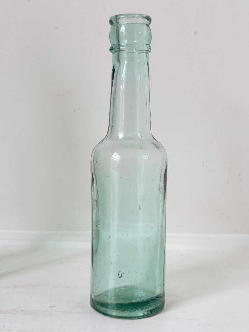 Trio of antique aqua and green glass bottles with embossed lettering, photographed on a white surface