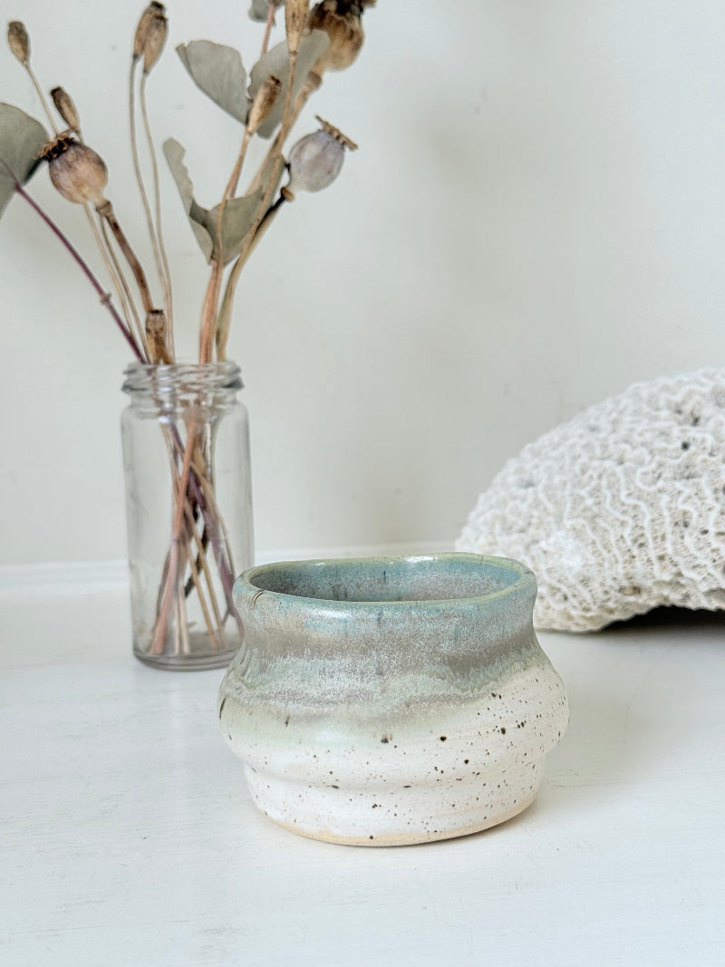 Studio pottery olive pot with soft green and cream glaze, photographed on a white surface