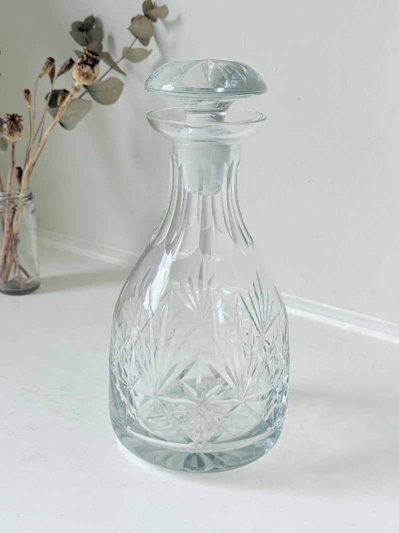 Vintage crystal decanter with faceted stopper and cut glass starburst design, photographed on a white surface
