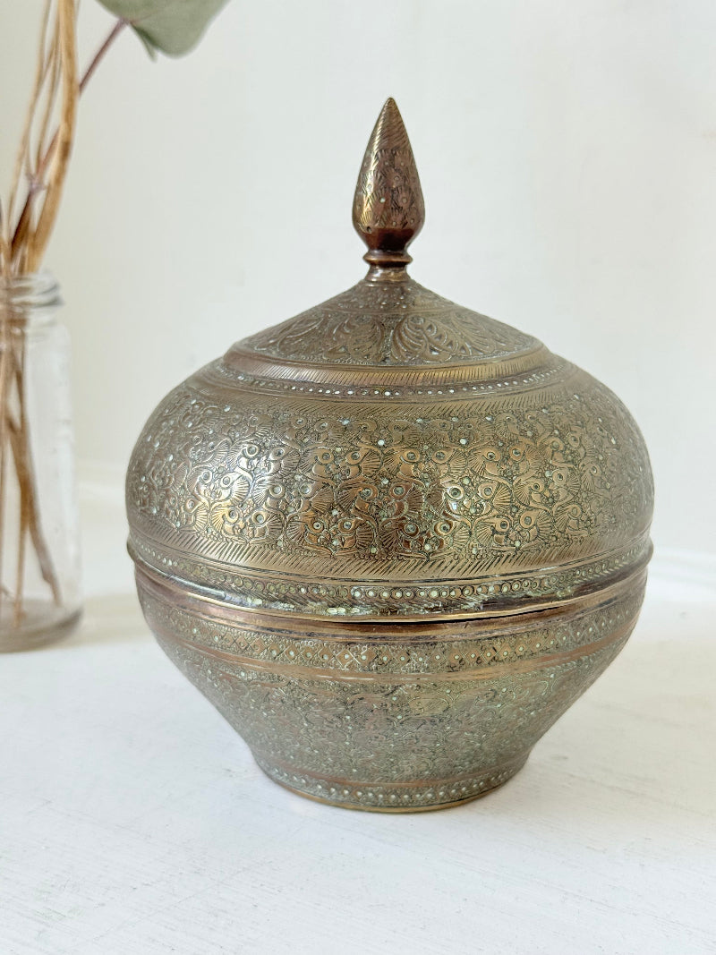 Indian Benares brass lidded jar with floral engraving and finial, photographed on a white surface