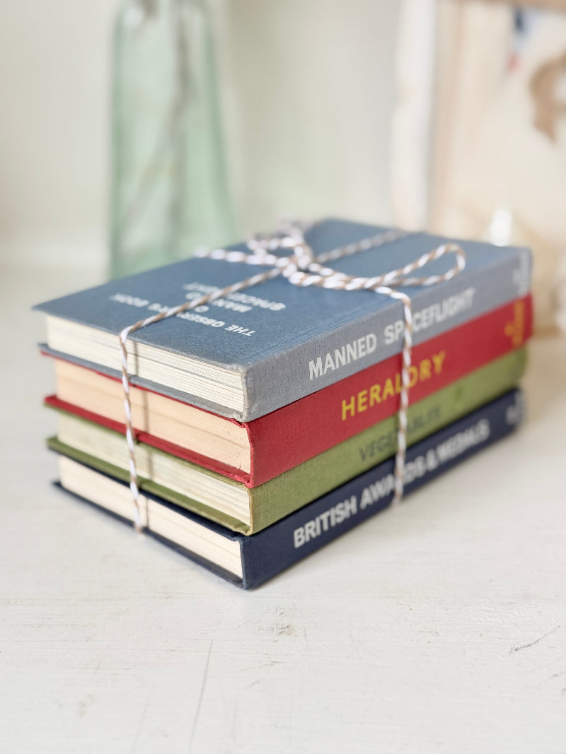A stack of four miniature hardcover books tied together with white string, featuring titles including &