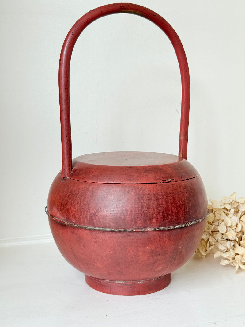 Vintage red painted wooden basket with tall curved handle and domed lid photographed on a white surface