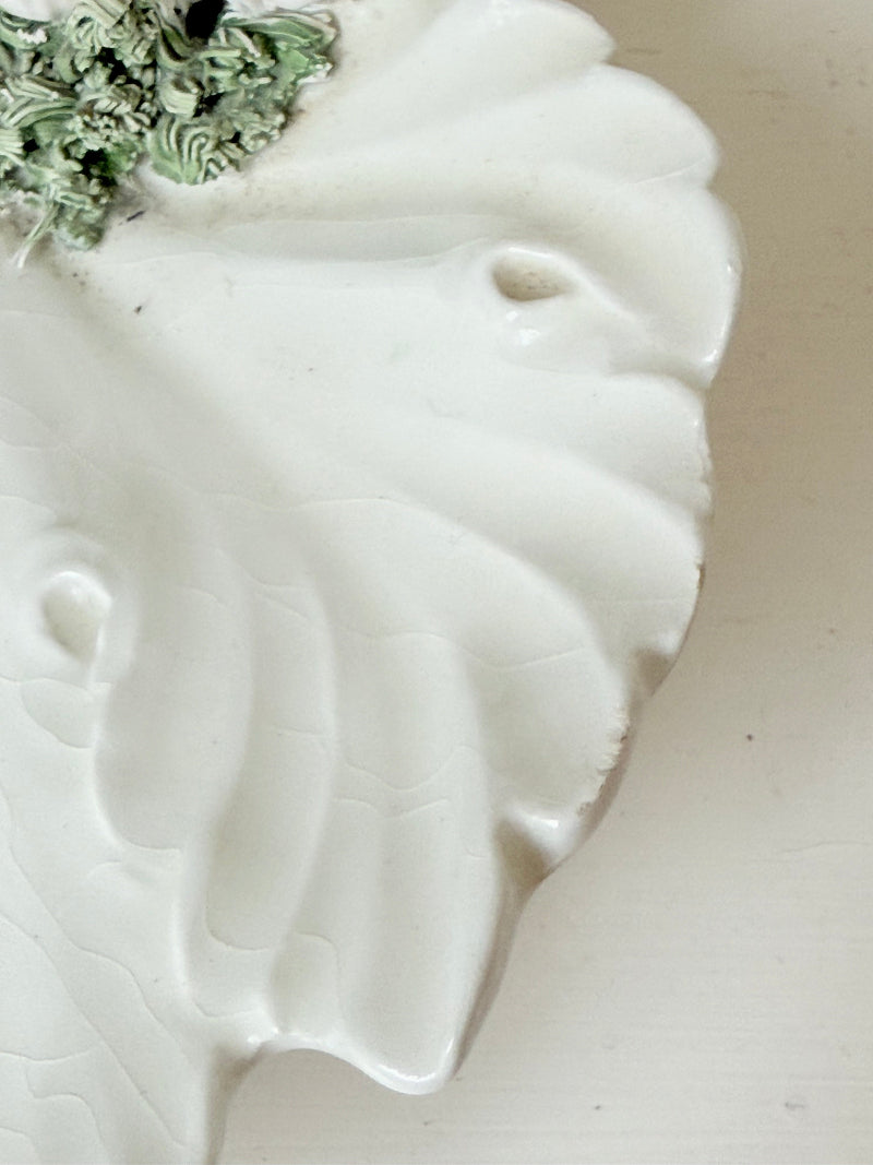 Italian ceramic dish featuring two white dogs on a sculpted leaf base, photographed on a white surface.