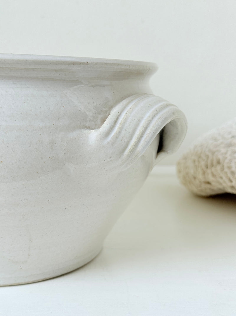 Large studio pottery bowl with hand-painted grape motif and side handles, photographed on a white surface