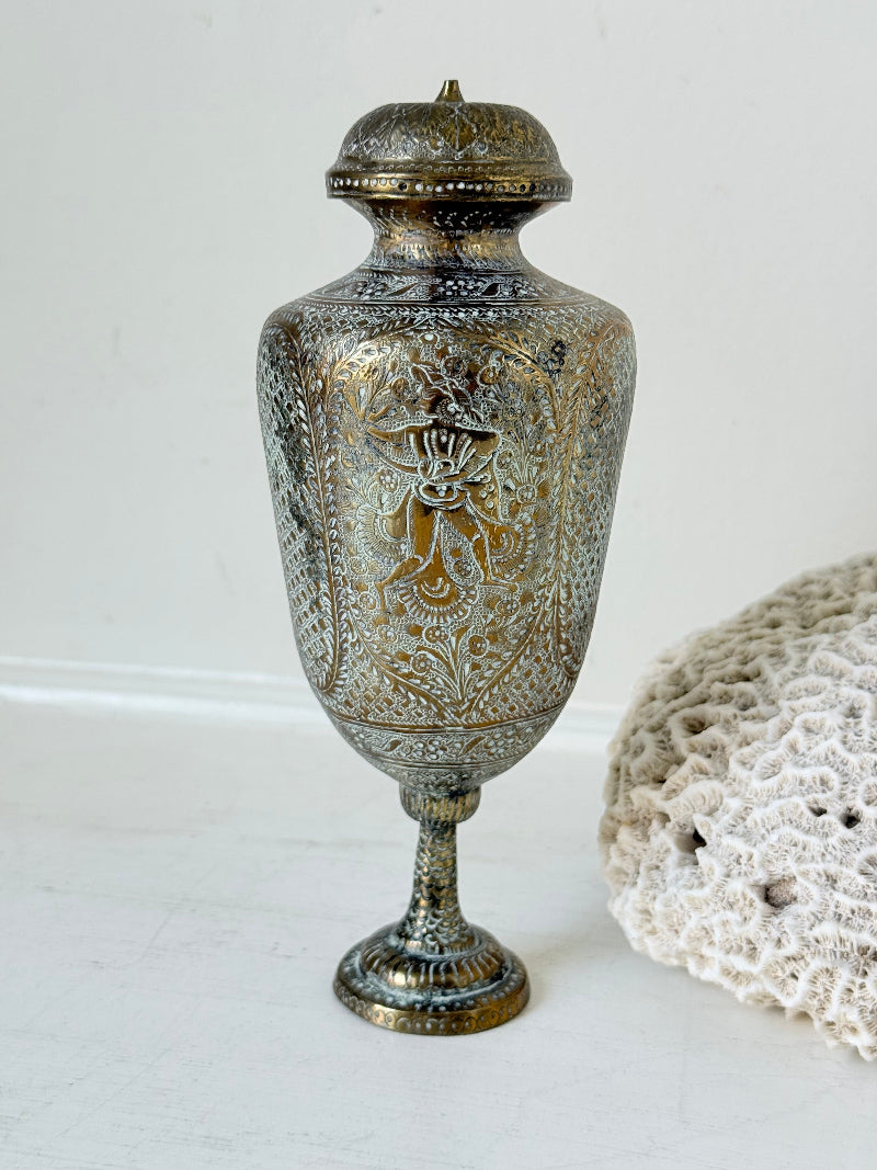 Indian Benares brass lidded vase with engraved figures and pedestal base, photographed on a white surface