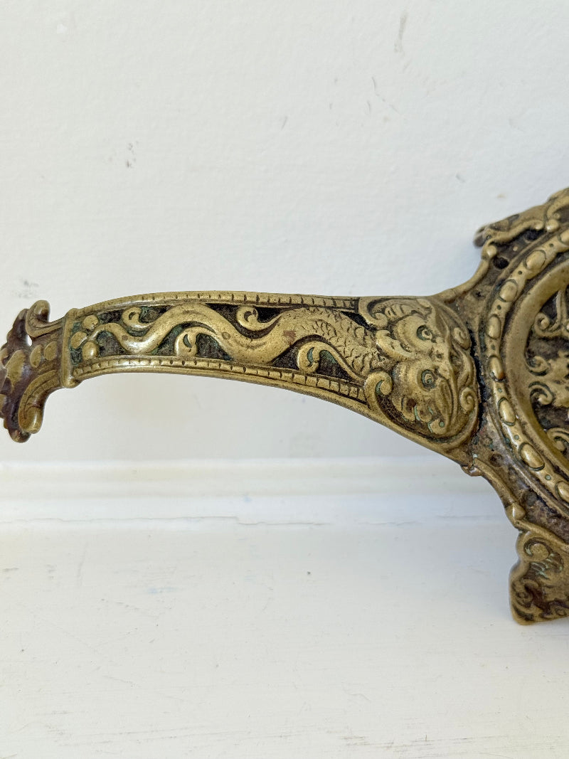 Ornate vintage brass candlestick with decorative handle and footed base, photographed on a white surface