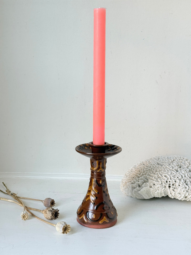 Vintage studio pottery candlestick in brown glaze with cut out decoration styled with coral taper candle on white surface