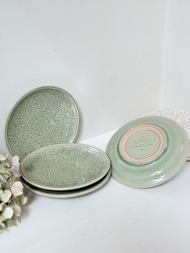 Set of four Thai celadon side plates with embossed patterns and sage green crackled glaze, stacked and photographed on white surface