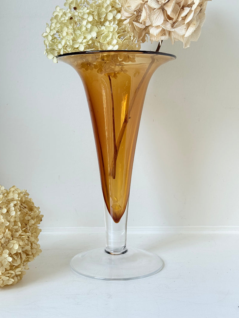 Tall mid-century amber trumpet vase with flared rim and clear glass foot, styled against a neutral background